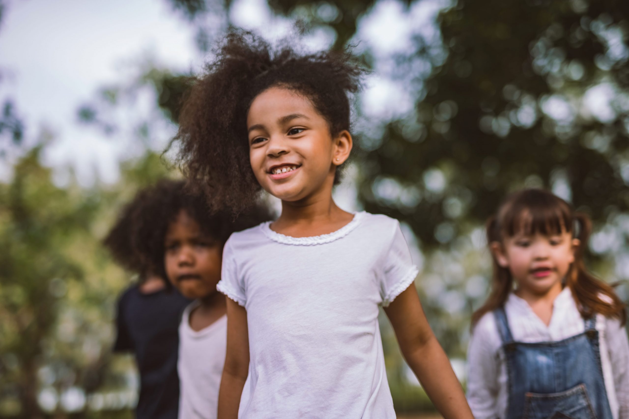 Three children are playing outside and smiling.