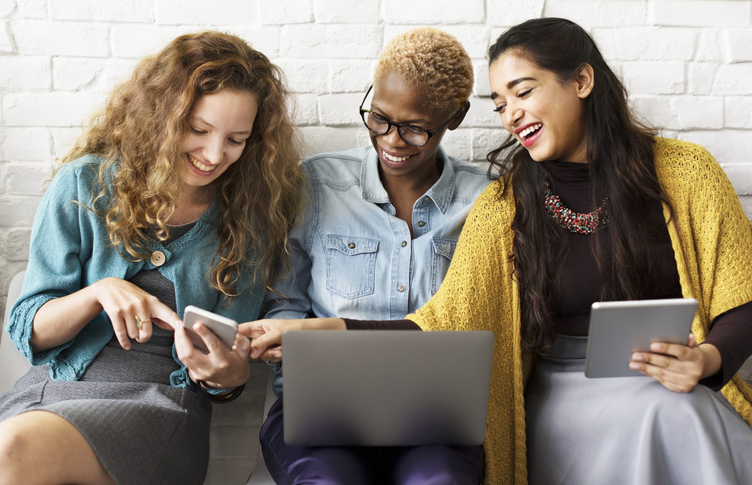 Three women sit together comparing notes on their devices.