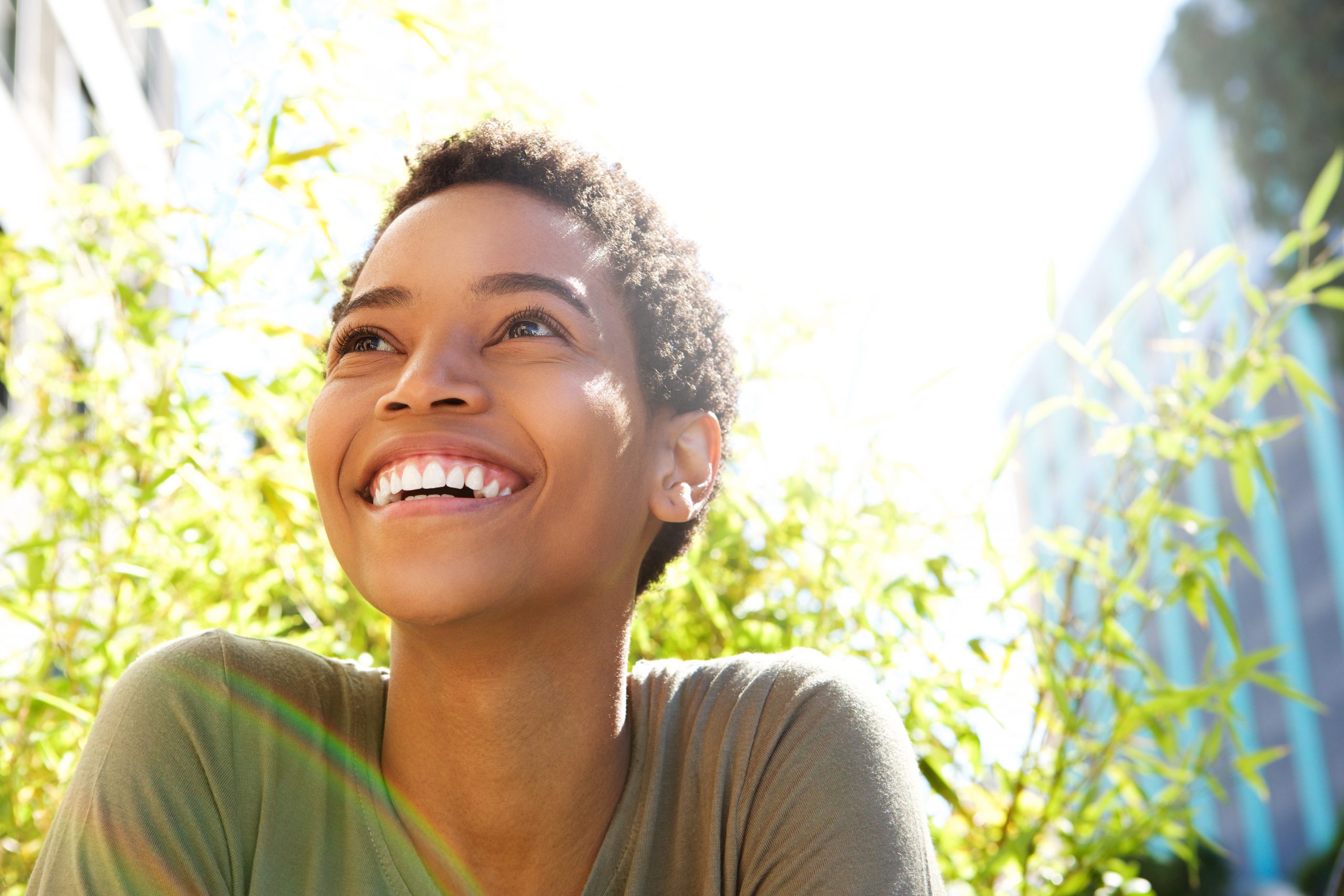 A woman looks up toward a sunny sky, smiling at what the future holds.