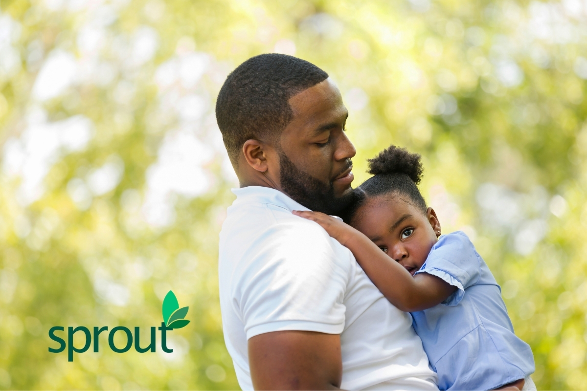 A Black father holds his little girl, who lays against his chest in pigtails.