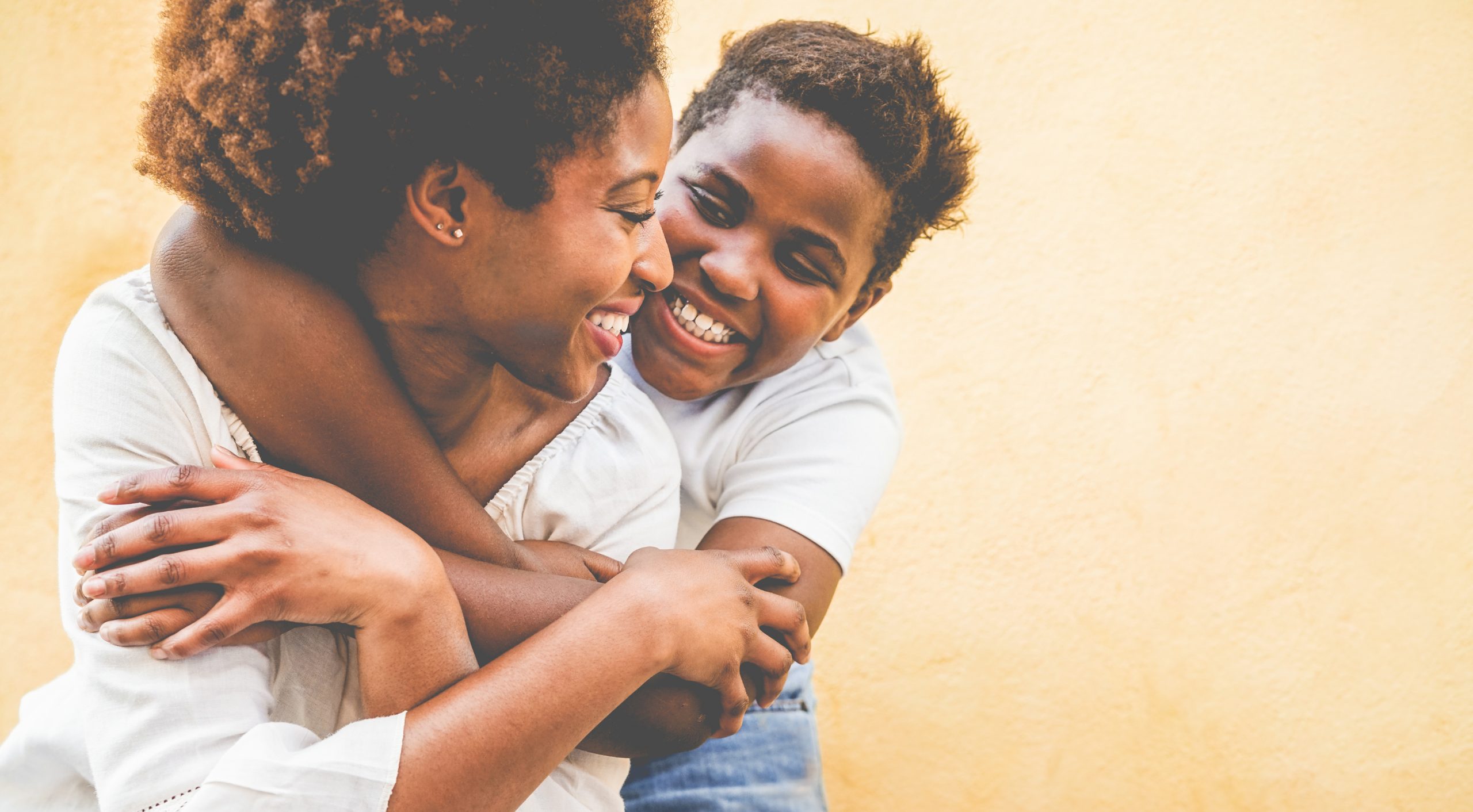 A child hugs his mom from behind.