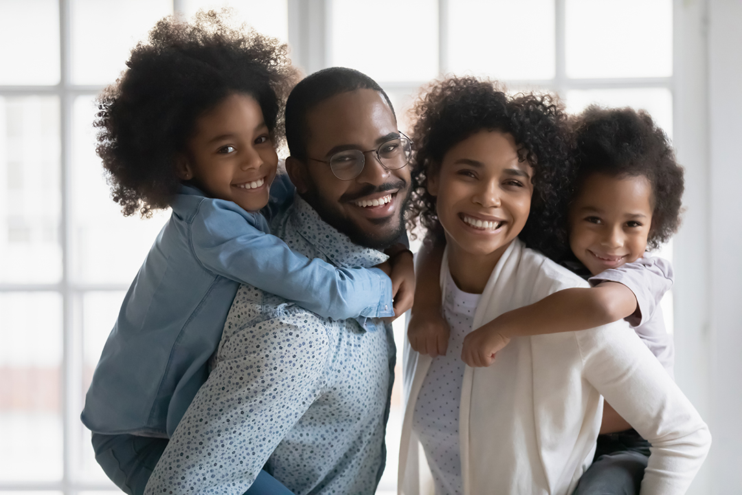 Portrait of Black parents giving their kids a piggy back ride.