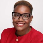 Karen Freeman-Wilson Karen is a black women with short hair. She is wearing bold glasses and a red top.