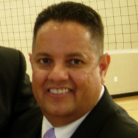 Julio is sitting at a table during an event, smiling and wearing a suit.