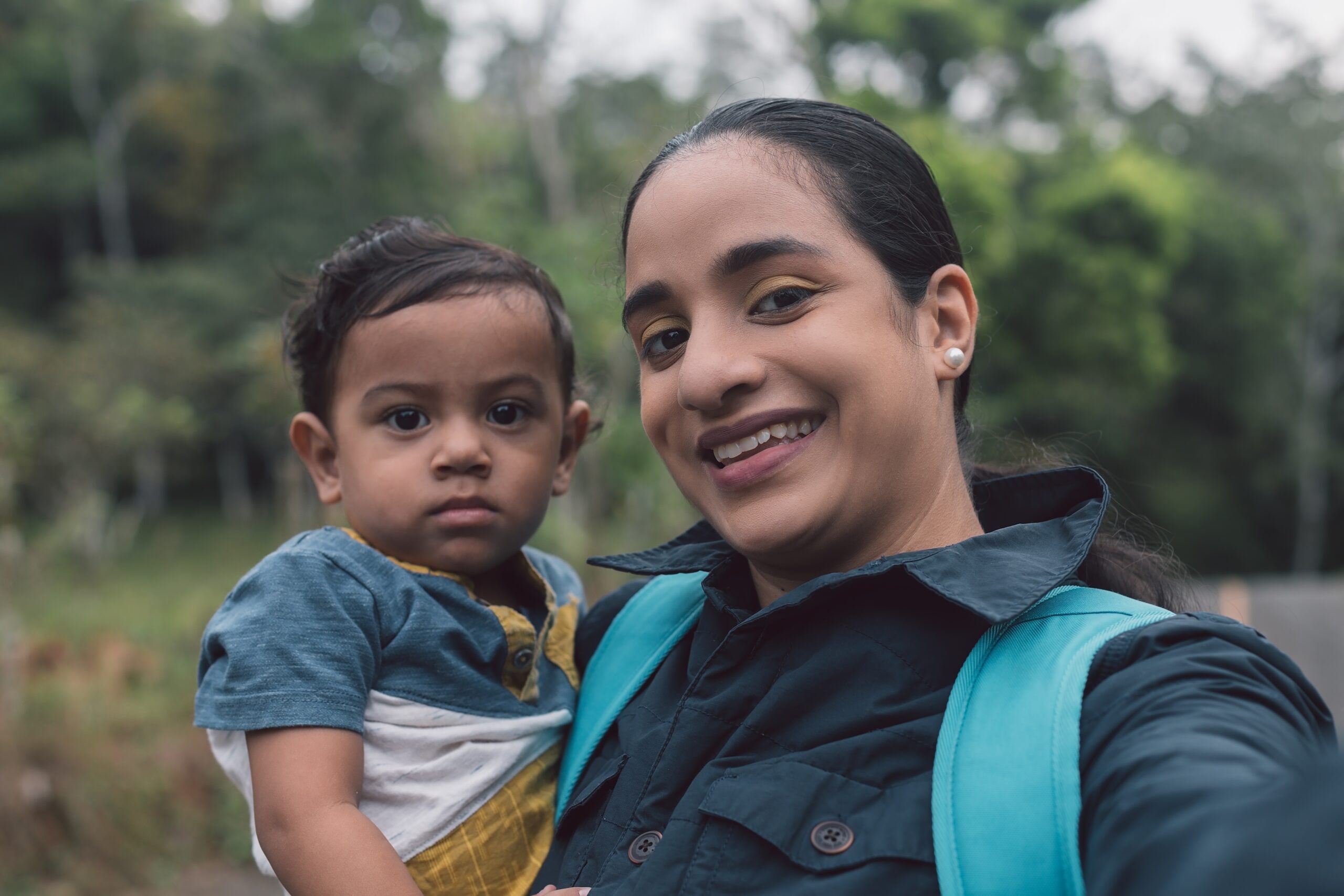 A Latina mom and her child stand in the woods taking a selfie.