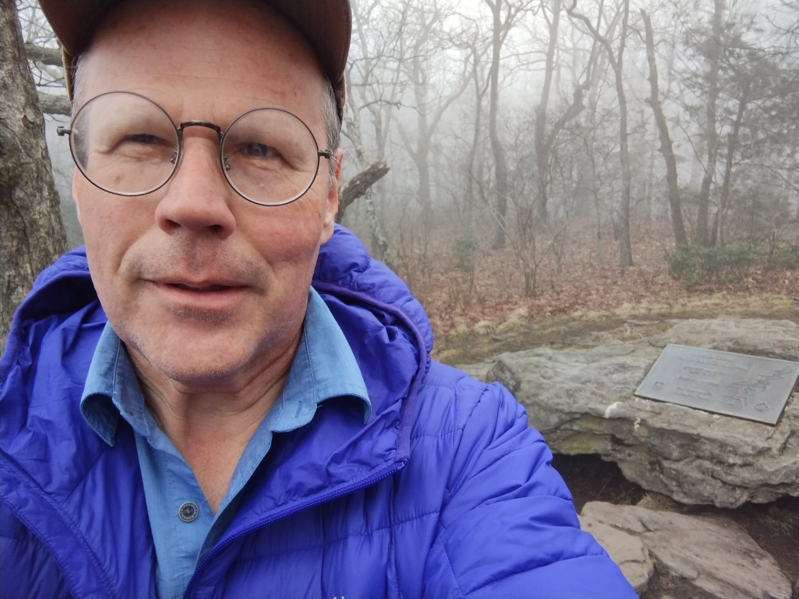 Steve is a white, older man standing in a foggy forest while on his hike.
